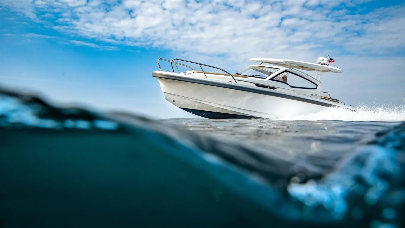 A white motorboat speeds through water under a blue sky with clouds, creating splashes as it moves.